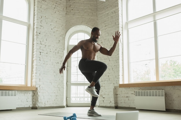 Giovane uomo afro-americano allenamento a casa, facendo esercizi di fitness, aerobica.