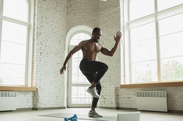 Young african-american man training at home , doing exercises of fitness, aerobic.