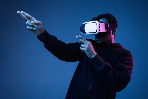 Young african-american man in VR-glasses in neon on blue