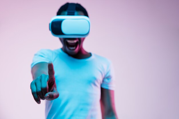 Young african-american man in VR-glasses in neon light on gradient