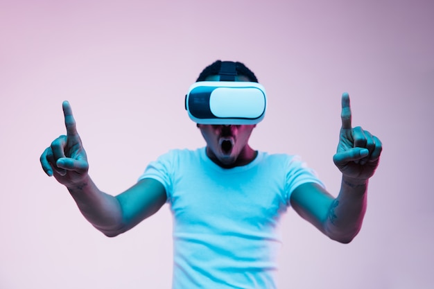 Young african-american man in VR-glasses in neon light on gradient