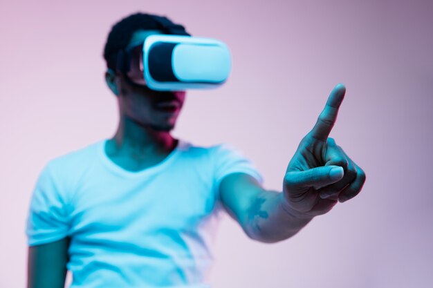 Young african-american man in VR-glasses in neon light on gradient