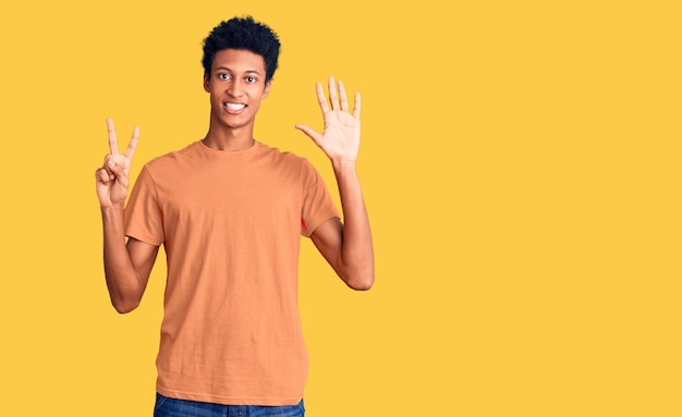 Foto gratuita giovane uomo afroamericano che indossa abiti casual mostrando e indicando con le dita numero sette mentre sorride fiducioso e felice