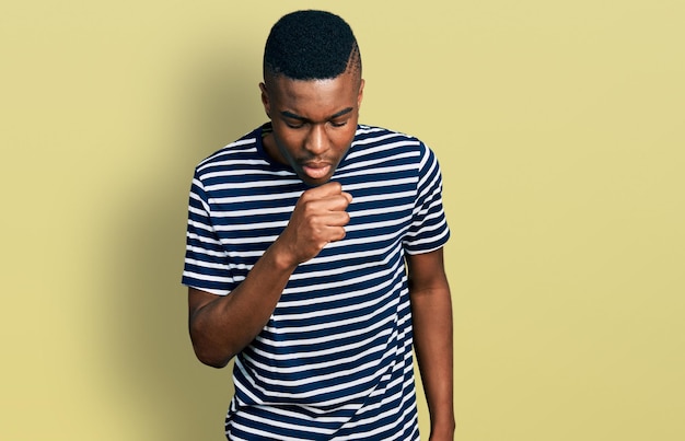 Young african american man wearing casual striped t shirt feeling unwell and coughing as symptom for cold or bronchitis health care concept