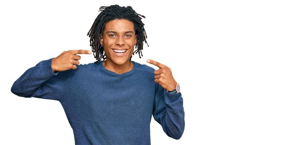 カジュアルな冬のセーターを着た若いアフリカ系アメリカ人男性が、笑顔を見せ、指で歯と口の歯科医療のコンセプトを指差す