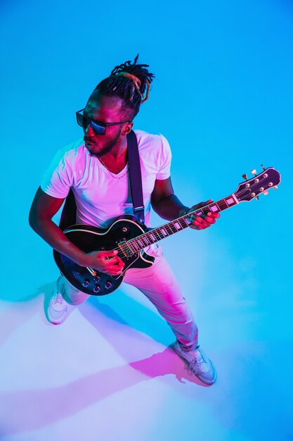 네온 불빛에 파란색 벽에 록 스타처럼 기타를 연주하는 젊은 아프리카 계 미국인 음악가.