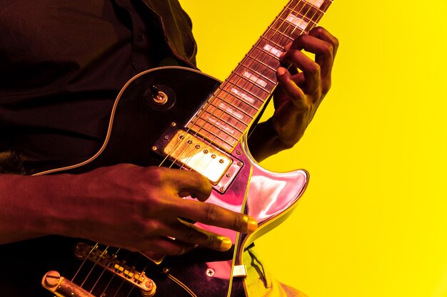 네온 불빛에 노란색 바탕에 록 스타처럼 기타를 연주하는 젊은 아프리카 계 미국인 음악가.