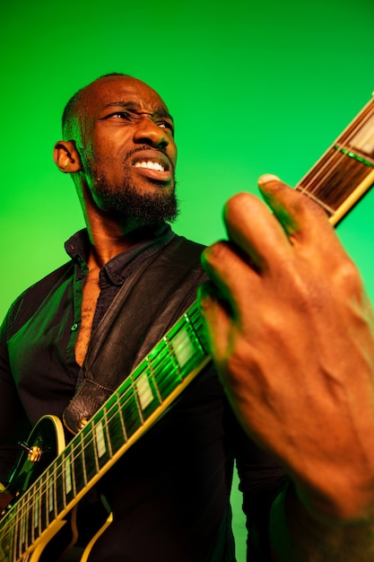 그라데이션 녹색 노란색 벽에 록 스타처럼 기타를 연주하는 젊은 아프리카 계 미국인 음악가.