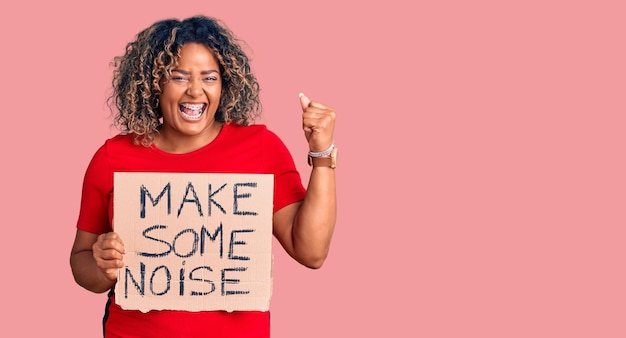 Free photo young african american plus size woman holding make some noise banner screaming proud celebrating victory and success very excited with raised arms