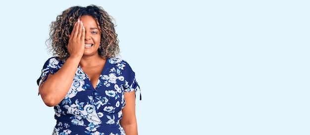 Young african american plus size woman wearing casual clothes covering one eye with hand confident smile on face and surprise emotion