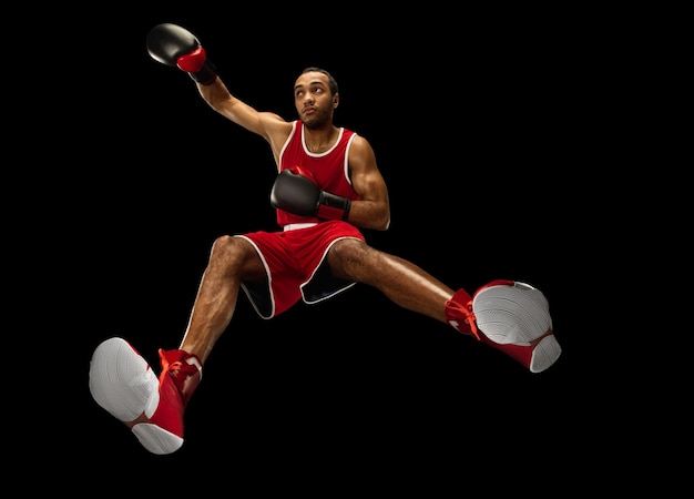 Young african-american professional boxer in action, motion isolated on black background