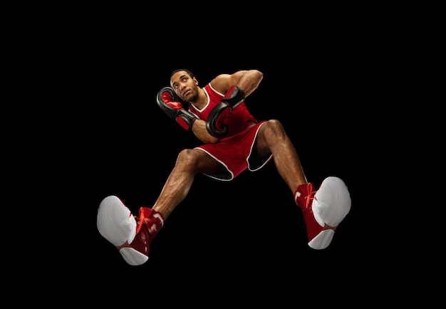Молодой афро-американский профессиональный боксер в действии, движение, изолированное на черной стене, взгляд снизу. Понятие спорта, движения, энергии и динамичного, здорового образа жизни. Обучение, практика.