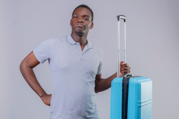 Молодой афро-американский путешественник в серой рубашке поло с синим чемоданом недоволен и хмурится