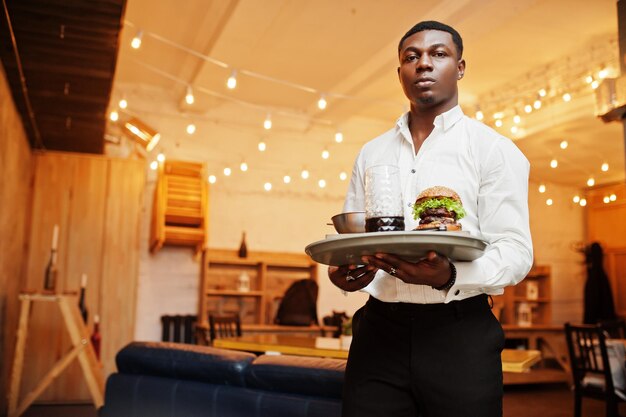 Молодой афро-американский официант держит поднос с гамбургером в ресторане