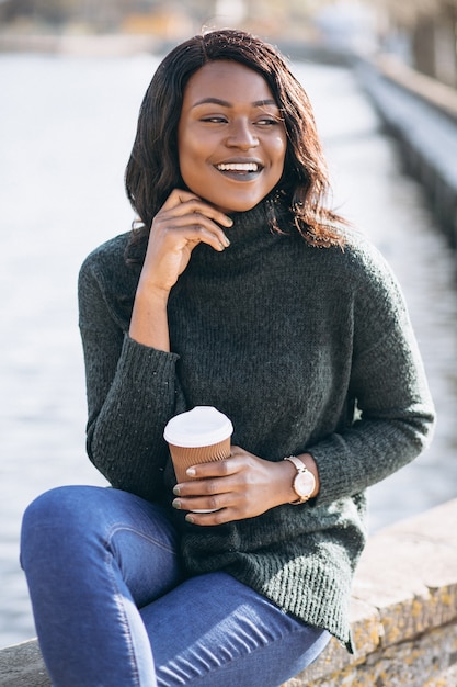 Молодая афроамериканец женщина пьет кофе у озера