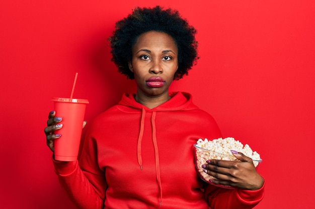 Free photo young african american woman eating popcorn and drinking soda relaxed with serious expression on face. simple and natural looking at the camera.