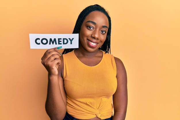 Foto gratuita giovane donna afroamericana che tiene carta da lettere commedia che sembra positiva e felice in piedi e sorride con un sorriso sicuro che mostra i denti