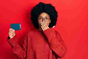 Free photo young african american woman holding ssd memory covering mouth with hand, shocked and afraid for mistake. surprised expression