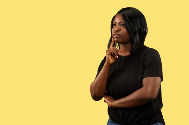 Young african-american woman isolated on yellow  space, facial expression. Beautiful female half-length portrait.