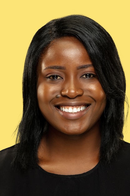 Young african-american woman isolated on yellow studio background, facial expression. Beautiful female close up portrait. Concept of human emotions, facial expression. Smiling, keeping calm.