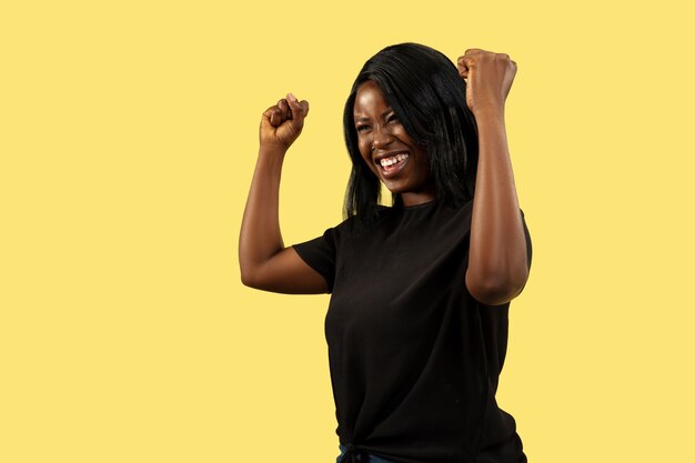 Young african-american woman isolated on yellow studio background, facial expression. Beautiful female half-length portrait. Concept of human emotions, facial expression. Crazy happy, celebrating.