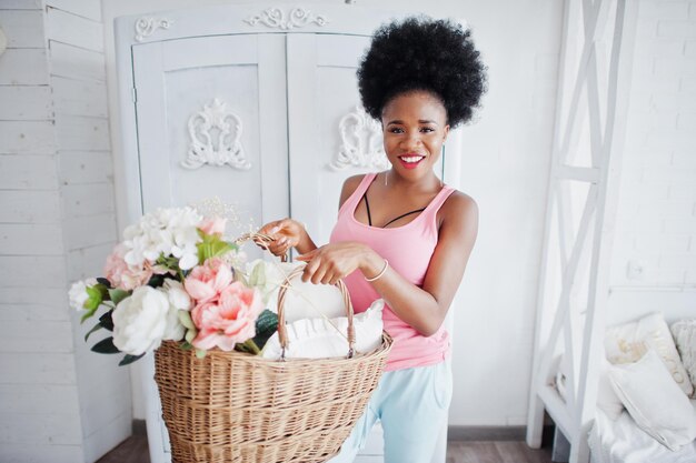 Молодая африканская американка в розовой майке с корзиной цветов в своей комнате