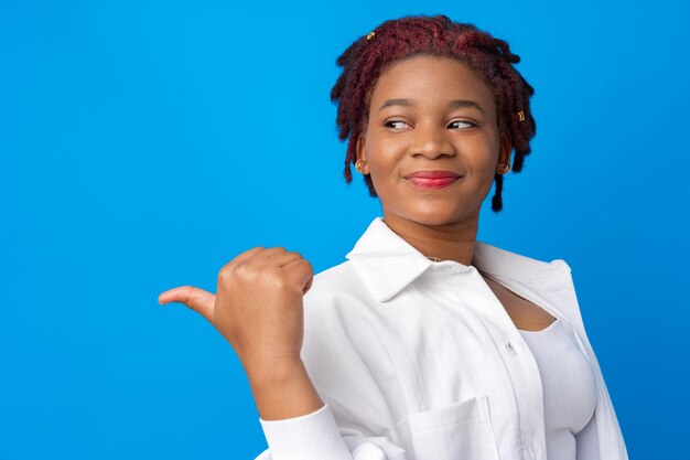 Young african american woman pointing to copy space against blue background