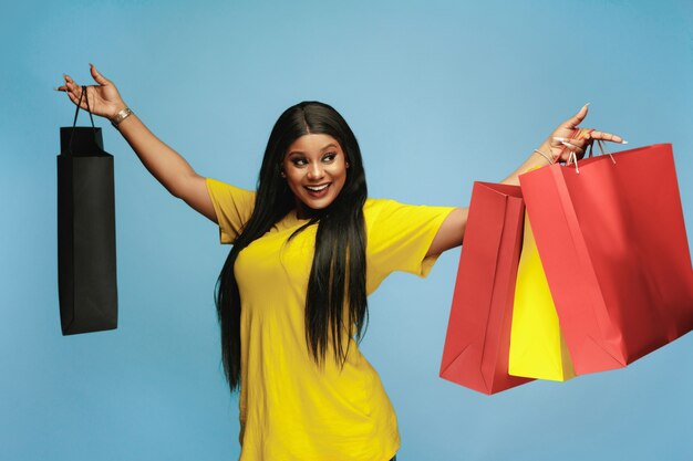 Young african-american woman shopping with colorful packs on blue background. Attractive female model.