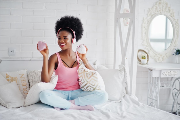 Young african american woman sitting in bed and listen music on earphones