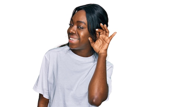 Free photo young african american woman wearing casual white t shirt smiling with hand over ear listening an hearing to rumor or gossip deafness concept