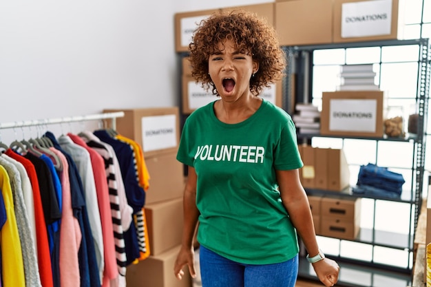 Free photo young african american woman wearing volunteer t shirt at donations stand angry and mad screaming frustrated and furious shouting with anger rage and aggressive concept