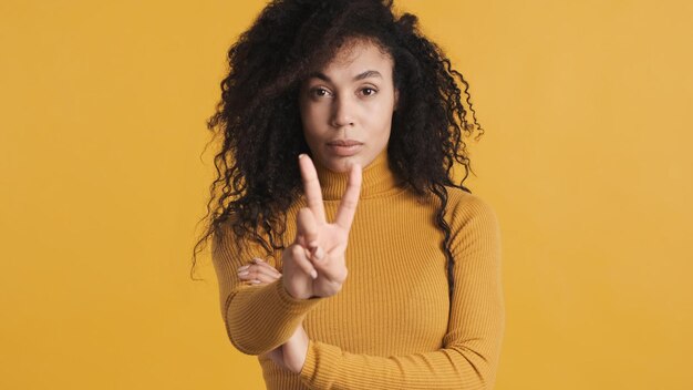 검은색 솜털 머리를 가진 젊은 아프리카계 미국인 여성은 노란색 배경 두 손가락에 격리된 손가락으로 자신감 있게 세고 있습니다.