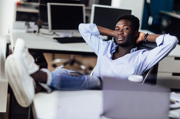 彼のオフィスでリラックスしている若いアフリカのビジネスマン。仕事を終えて休憩する時間。