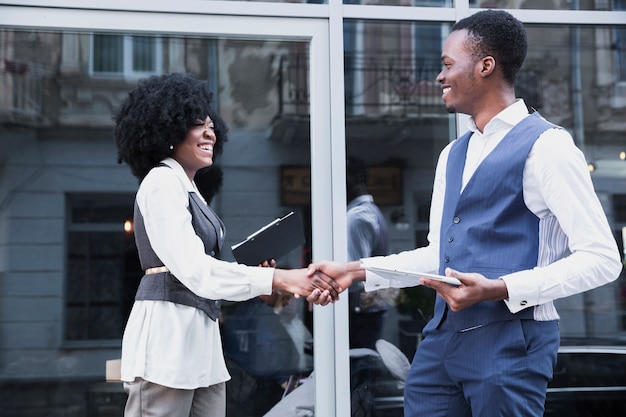 Young african businessman and businessman shaking hand in front of glass window