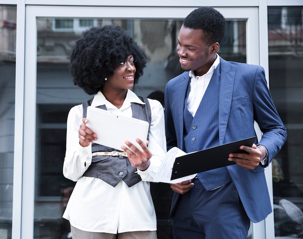 Free photo young african businessman and businesswoman holding digital tablet and clipboard looking at each other