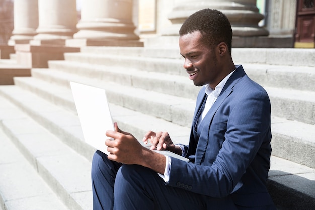 Young african businessman sitting on steps using laptop at outdoors