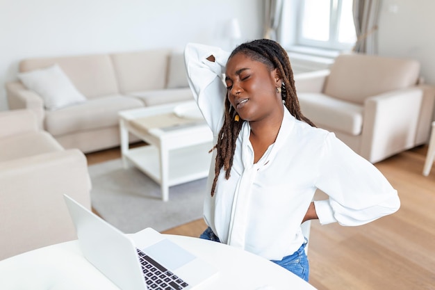 オフィスの机に座っている間に背中の痛みを抱えている若いアフリカの実業家オフィスの机でラップトップに取り組んでいる間彼女を保持している実業家