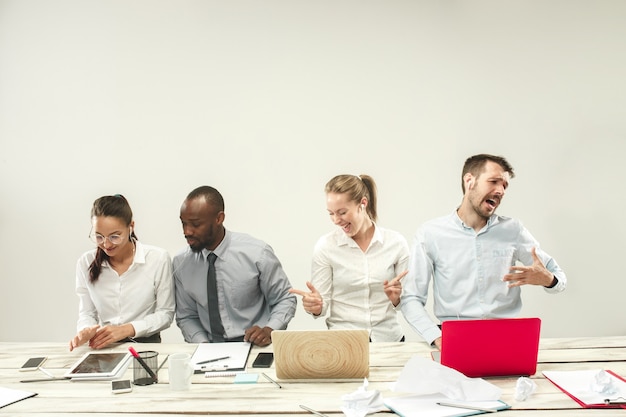 Free photo young african and caucasian men and women sitting at office and working on laptops. the business, emotions, team, teamwork, workplace, leadership, meeting concept. different emotions of colleagues