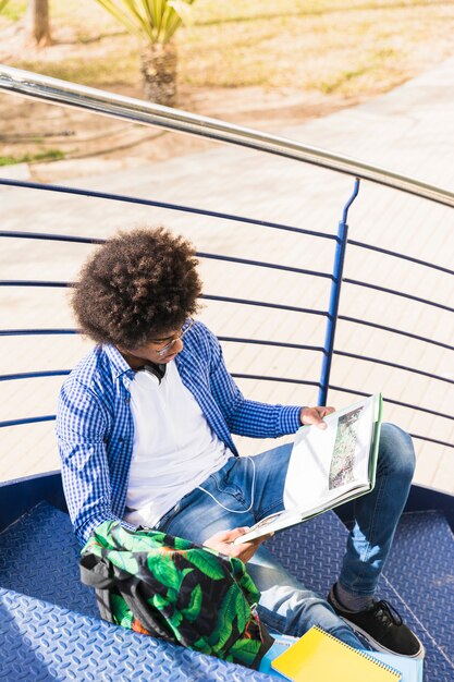 Молодой африканский студент сидя на лестнице читая книгу