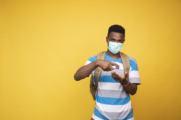 Young African male wearing a facemask and using a hand sanitizer - COVID-19