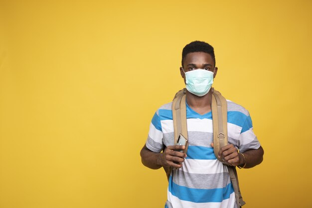 フェイスマスクを身に着けているバックパックを持つ若いアフリカの男性-COVID-19