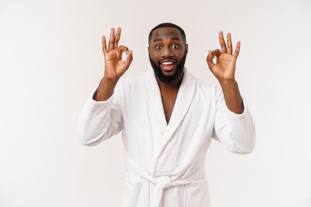 Young African man in bathrobe prepare for skin care showing ok finger sign Human emotions concept