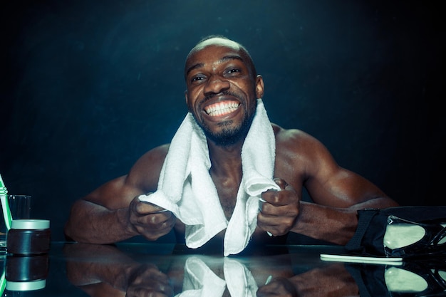 The young african man in bedroom sitting in front of the mirror after scratching his beard at home. Human emotions concept