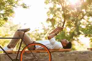 Foto gratuita primo mattino del giovane uomo africano con la bicicletta all'aperto facendo uso della compressa