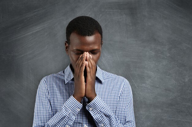 Young African man holding hands in prayer, trying to calm down , thinking of something bad, hoping for the best.