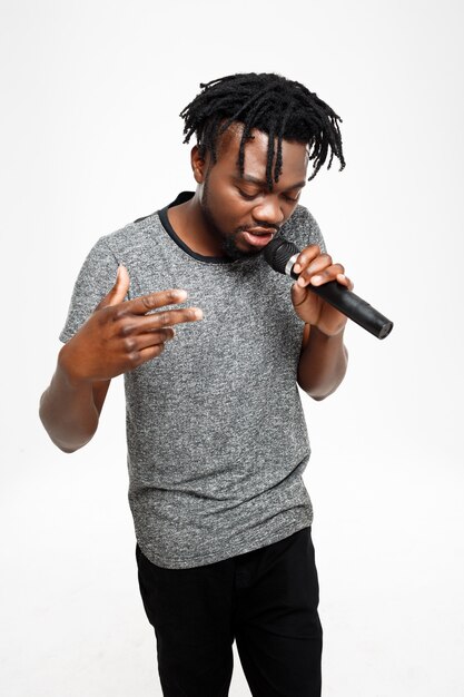 Young african man singing in microphone on white.