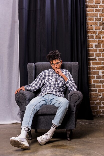 Young african man sitting on chair in front of curtain looking at camera