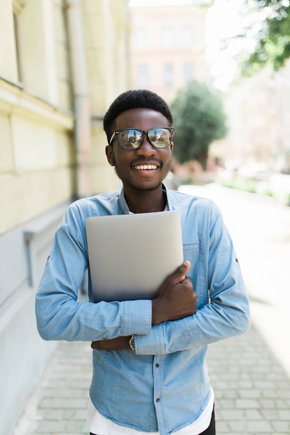 Молодой африканский человек, стоящий на праздновании успеха на улице, глядя на свой ноутбук в руке