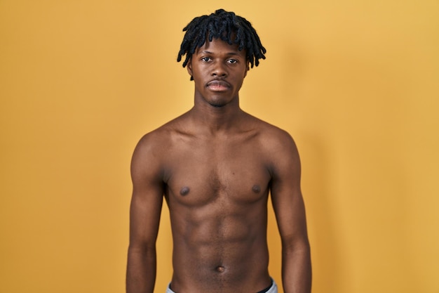 無料写真 上半身裸で立っているドレッドヘアを持つ若いアフリカ人は、顔に真剣な表情でリラックスしました。シンプルで自然なカメラ目線。