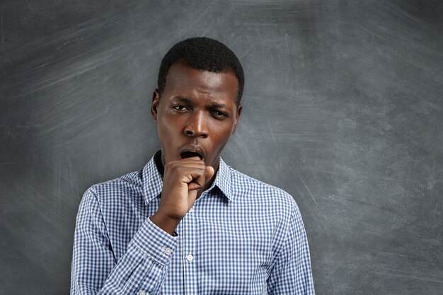 Young African teacher looking tired and sleepy, yawning, covering his mouth with, after sleepless night. Black student looking bored and disinterested during math class at university.